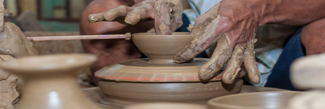man shapes pottery as it turns on a wheel